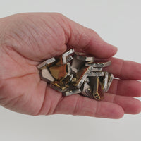 Video of Flip ceramic puzzle pieces in gold, opaque glazed porcelain, 4–20 mm, held in a hand and poured out to show their shapes and finish