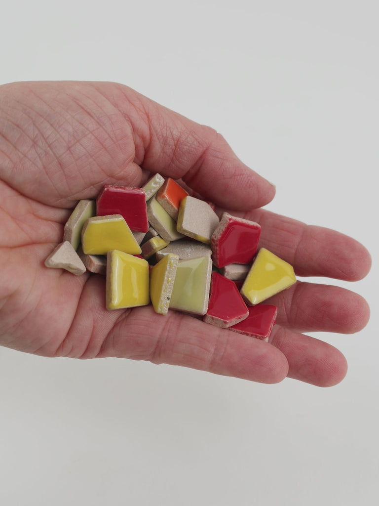 Video of Flip ceramic puzzle pieces in red mix, opaque glazed porcelain, 4–20 mm, held in a hand and poured out to show their shapes and finish
