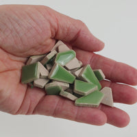 Video of Flip ceramic puzzle pieces in reed green, opaque glazed porcelain, 4–20 mm, held in a hand and poured out to show their shapes and finish