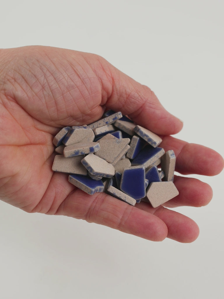 Video of Flip ceramic puzzle pieces in cobalt, opaque glazed porcelain, 4–20 mm, held in a hand and poured out to show their shapes and finish