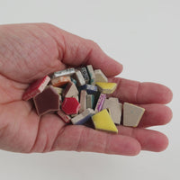 Video of Flip ceramic puzzle pieces in tropical mix, opaque glazed porcelain, 4–20 mm, held in a hand and poured out to show their shapes and finish