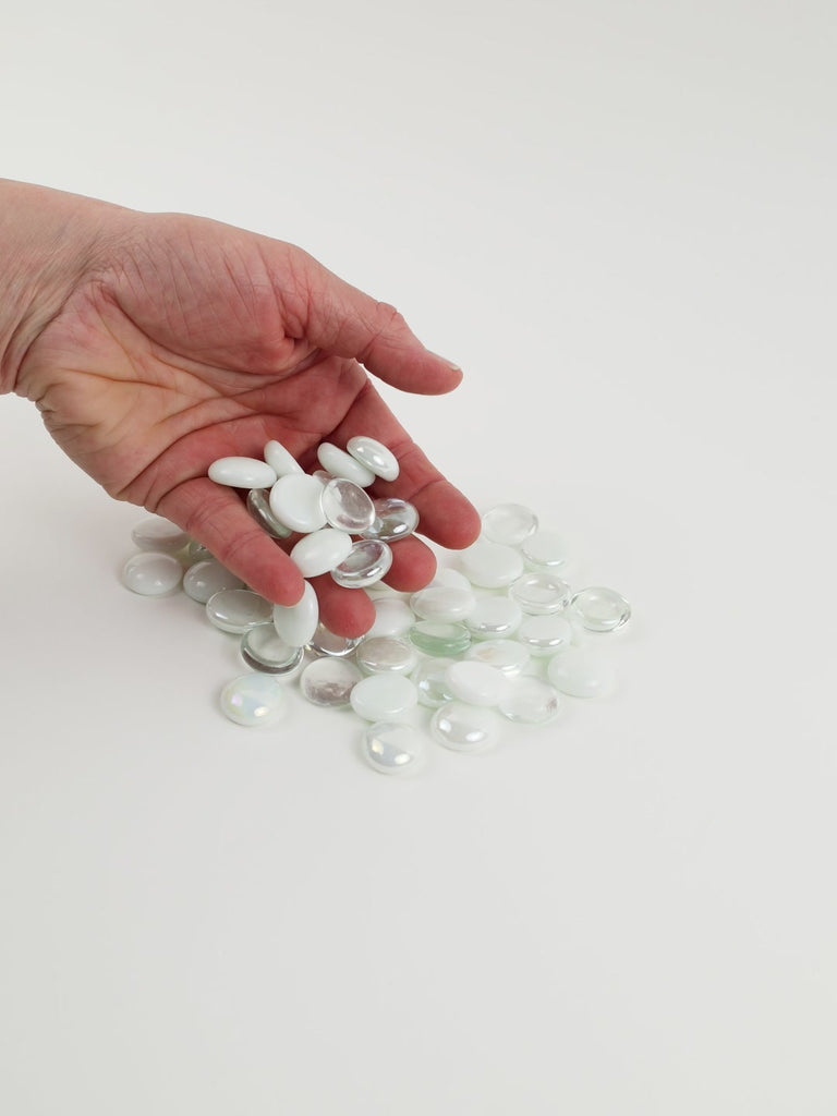 Video of white mix glass nuggets in white, frosted and clear shades with an iridescent sheen, 16–20 mm, picked up from a pile by hand and dropped back to show their size, round shape and shine
