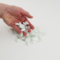 Video of white mix glass nuggets in white, frosted and clear shades with an iridescent sheen, 16–20 mm, picked up from a pile by hand and dropped back to show their size, round shape and shine