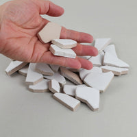 Video of Flip XL ceramic puzzle pieces in white, opaque glazed porcelain, 20–60 mm, picked up from a pile by hand and dropped back to show their size, shapes and finish