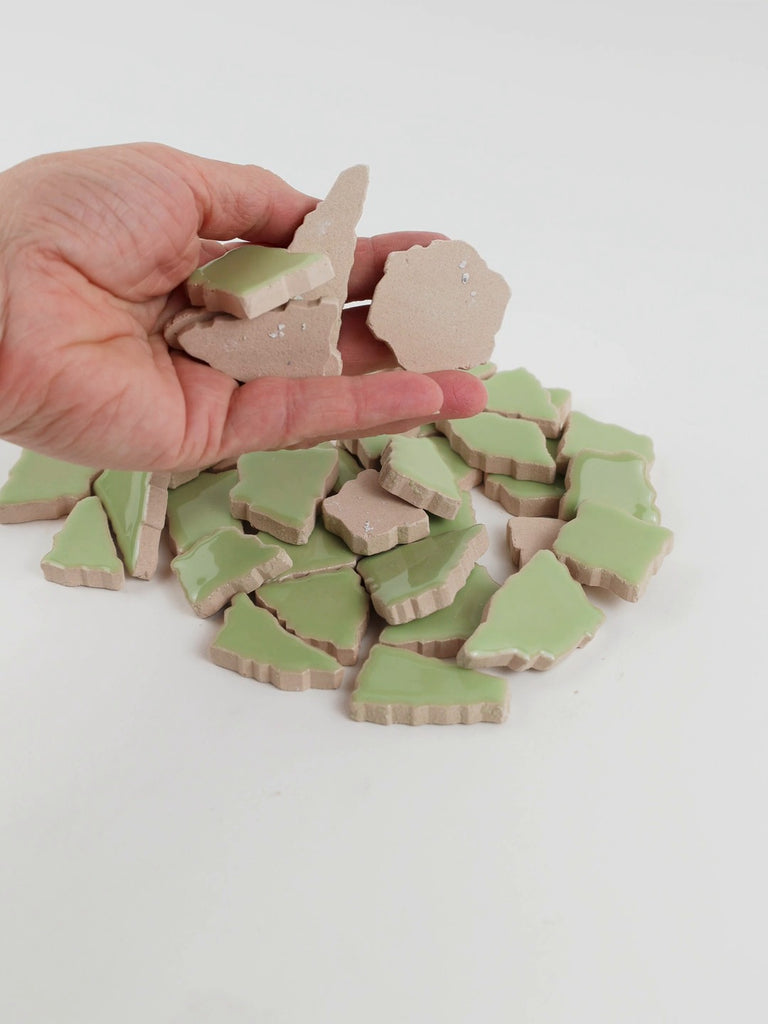 Video of Flip XL ceramic puzzle pieces in linden green, opaque glazed porcelain, 20–60 mm, picked up from a pile by hand and dropped back to show their size, shapes and finish