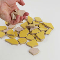 Video of Flip XL ceramic puzzle pieces in corn, opaque glazed porcelain, 20–60 mm, picked up from a pile by hand and dropped back to show their size, shapes and finish