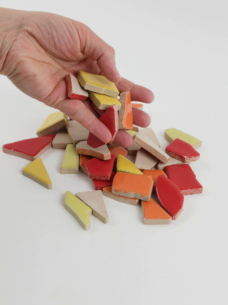Video of Flip XL ceramic puzzle pieces in red mix, opaque glazed porcelain, 20–60 mm, picked up from a pile by hand and dropped back to show their size, shapes and finish
