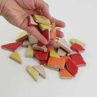 Video of Flip XL ceramic puzzle pieces in red mix, opaque glazed porcelain, 20–60 mm, picked up from a pile by hand and dropped back to show their size, shapes and finish