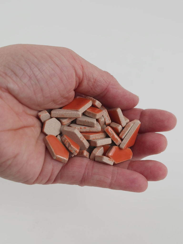 Video of Flip ceramic puzzle pieces in mandarin, opaque glazed porcelain, 4–20 mm, held in a hand and poured out to show their shapes and finish