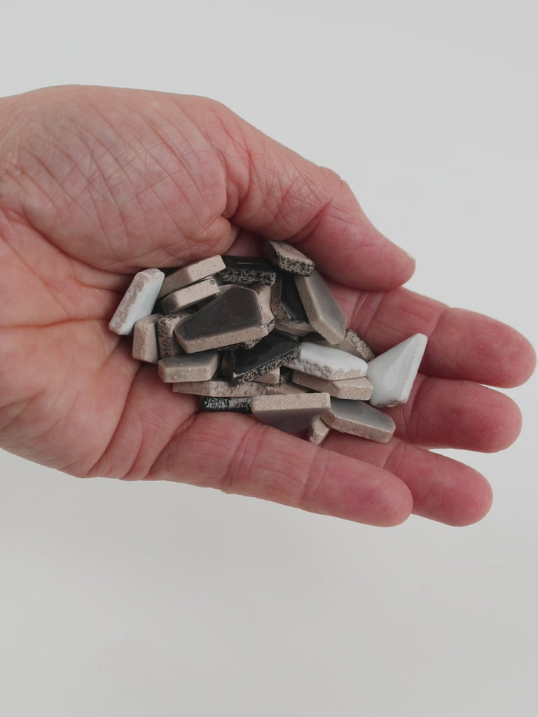 Video of Flip ceramic puzzle pieces in grey mix, opaque glazed porcelain, 4–20 mm, held in a hand and poured out to show their shapes and finish