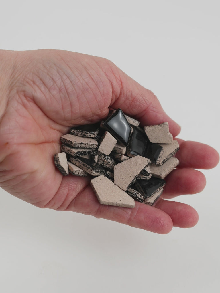Video of Flip ceramic puzzle pieces in black, opaque glazed porcelain, 4–20 mm, held in a hand and poured out to show their shapes and finish