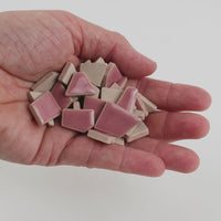 Video of Flip ceramic puzzle pieces in light pink, opaque glazed porcelain, 4–20 mm, held in a hand and poured out to show their shapes and finish