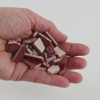 Video of Flip ceramic puzzle pieces in old pink, opaque glazed porcelain, 4–20 mm, held in a hand and poured out to show their shapes and finish