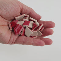 Video of Flip ceramic puzzle pieces in cherry red, opaque glazed porcelain, 4–20 mm, held in a hand and poured out to show their shapes and finish